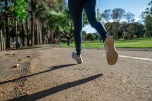 A woman running outdoors on a sunny day along a scenic park trail, focusing on fitness and health.